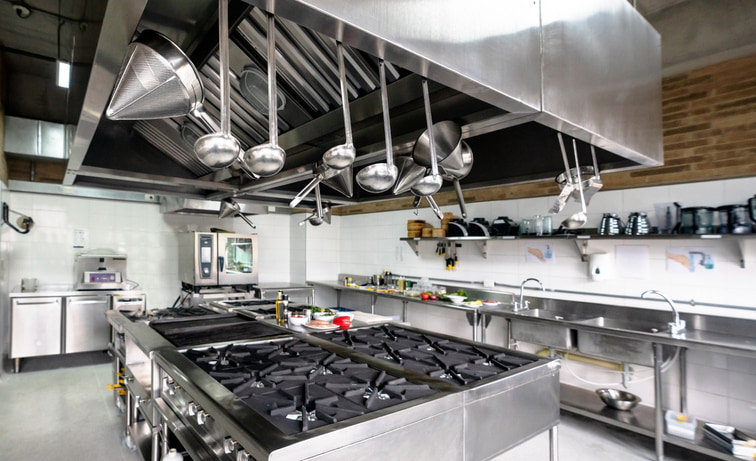 Commercial kitchen with large range in the middle and utensils hanging from the hood